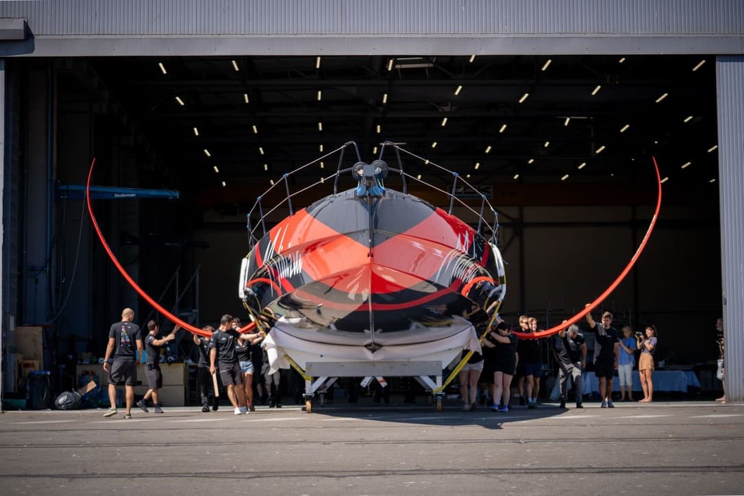 Bow view of the boat being moved out of the build shed, team members alongside